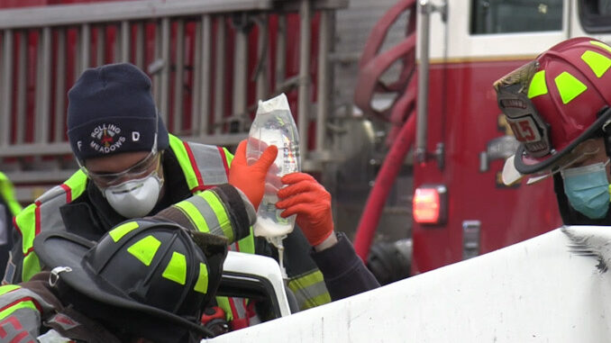 Firefighter/paramedics holding an IV bag during extrication of a crash victim from a severely-damaged vehicle on Algonquin Road just west of New Wilke Road near the border of Arlington Heights and Rolling Meadows