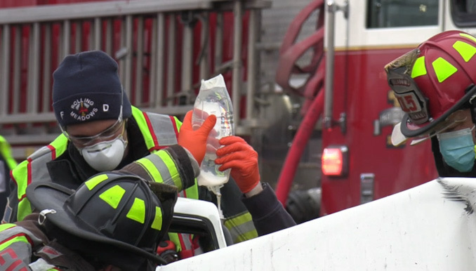 Firefighter/paramedics holding an IV bag during extrication of a crash victim from a severely-damaged vehicle on Algonquin Road just west of New Wilke Road near the border of Arlington Heights and Rolling Meadows