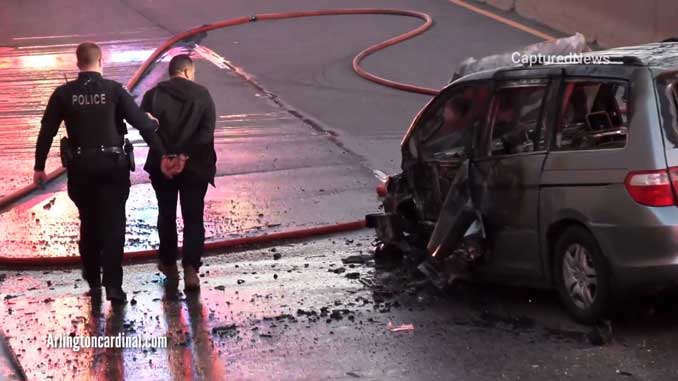 Wrong way driver is led in handcuffs past the destroyed and burned up minivan he was allegedly driving the westbound in the eastbound lanes of Palatine Road Saturday, May 1, 2021 