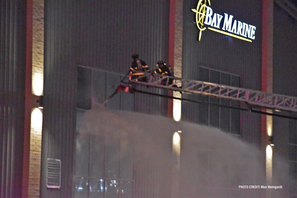 Firefighters using a master stream from a tower ladder aim into the building from an upper window at Bay Marine, 3 East Madison Street in Waukegan (PHOTO CREDIT: Max Weingardt)