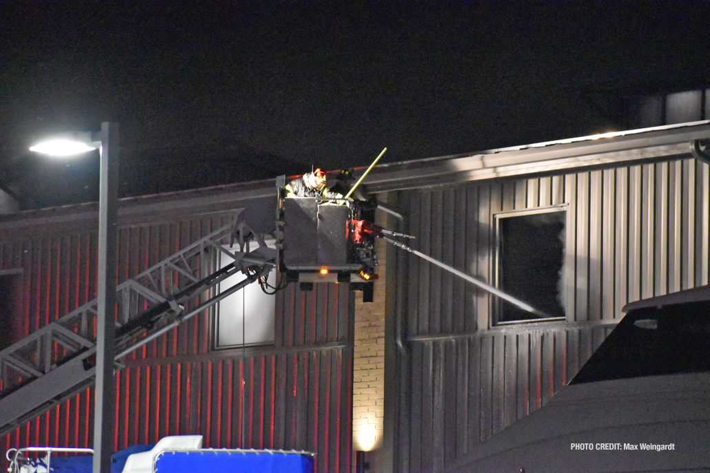 Firefighters using a master stream from a tower ladder aim into the building from an upper window at Bay Marine, 3 East Madison Street in Waukegan (PHOTO CREDIT: Max Weingardt)