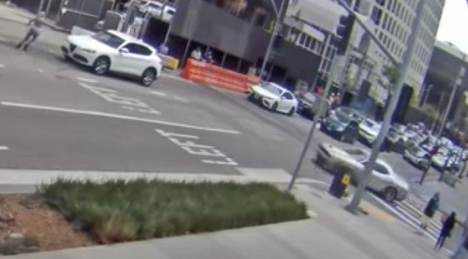 A female robbery victim runs and attempts to seek help and take cover on the far side of a white SUV while she points toward robbery offenders that are chasing her in a silver Dodge Challenger in the Jewelry District in downtown Los Angeles (SOURCE: Los Angeles Police Department)