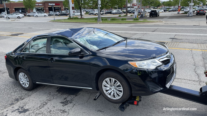 A black Toyota Camry with roof and windshield damage after a light pole that was struck by the red Volvo compact SUV dropped on the roof of the Toyota Camry