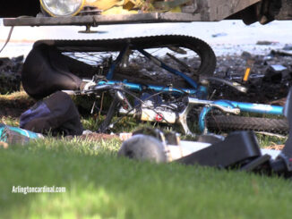 A damaged bicycle underneath the middle of a landscaping truck that was forced of the roadway by another vehicle