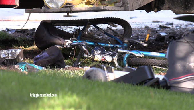 A damaged bicycle underneath the middle of a landscaping truck that was forced of the roadway by another vehicle