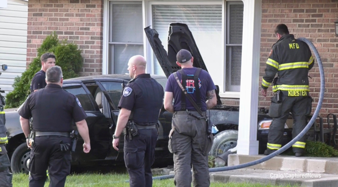 A Mundelein firefighter with a hose line inspects the engine compartment of a Ford Crown Victoria after a small occurred after a crash against a house in Mundelein (Craig/CapturedNews)