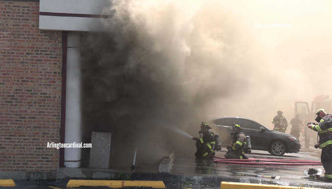 Firefighters direct a stream of water into the front of a store in a strip mall at the southeast corner of Elmhurst Road and Hintz Road in Prospect Heights (CARDINAL NEWS)