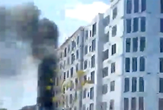 Smoke column and heat rise adjacent to a 7-story mixed-use building at The Clove development in Buffalo Grove as fire burned debris in an open top semi-trailer dumpster (frame from provided cell phone video)