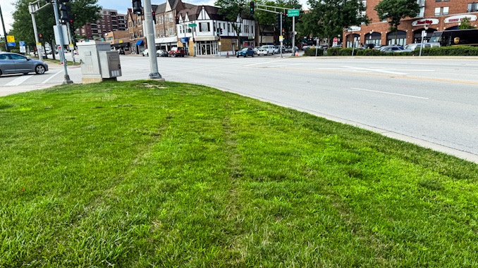 Tire tracks in the grass leading up to the impact site where a vehicle ramming crash damaged the flagstone sitting wall under the letter 'T' and 'S' Tuesday, July 29, 2025 (CARDINAL NEWS)