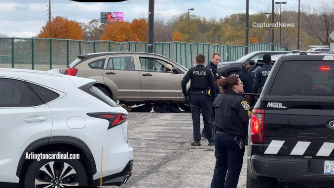 A woman facedown underneath her vehicle in a standoff with Metra and Arlington Heights police at the Arlington Park Metra Station parking lot Sunday morning, November 9, 2025 (CARDINAL NEWS)