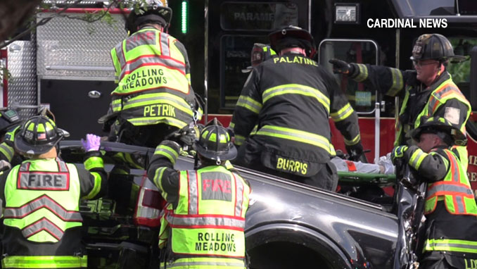 After cutting away the metal roof of a pickup truck and cutting away other materials that trapped a crash victim, firefighters lift the crash victim strapped to a backboard at a crash scene at Algonquin Road and Magnolia Drive in Rolling Meadows, Tuesday, May 26, 2026 (CARDINAL NEWS)