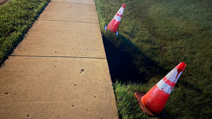 A few hours after a dangerous sinkhole that was hard to detect at night was reported by CARDINAL NEWS on Tuesday evening, July 7, 2026, Arlington Heights public works placed two cones next to the sinkhole, but left it exposed with a fall risk overnight until a tape barrier was placed around the sinkhole on Wednesday (CARDINAL NEWS).
