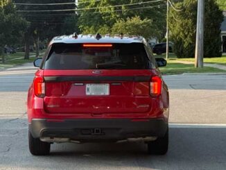 Unmarked red Ford Interceptor "flat top" (without a roof-mounted lightbar) with no official markings or designations, with an M-plate, which is a special registration plate assigned to vehicles owned and operated by local city or village governments, including municipal police vehicles, fire vehicles, public works vehicles, and of official vehicles for official use (CARDINAL NEWS)